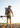 Man with a camouflage backpack and rifle walking through a field.