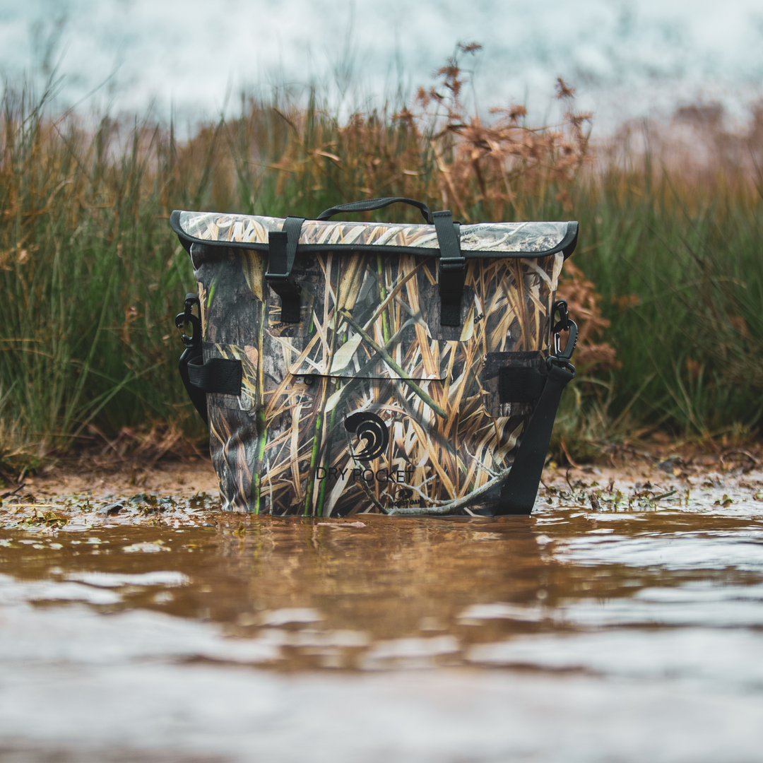Dry Pocket's Mossy Oak Camouflage-patterned universal waterproof, scent proof, and floating magnetic double lock auto-sealing 10 can tote cooler and dry bag with a shoulder strap on a white background