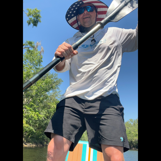 Man paddling a kayak wearing a pair of Dry Pocket waterproof shorts on a sunny day with trees in the background